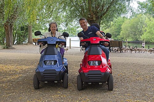 Photo of Councillor Beth Rowland and Councillor Mark Ashwell driving mobility scooters at Dinton Pastures Country Park
