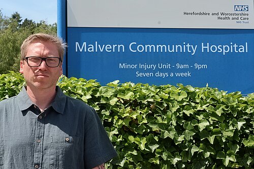 Cllr Dan, angry, next to Malvern NHS sign